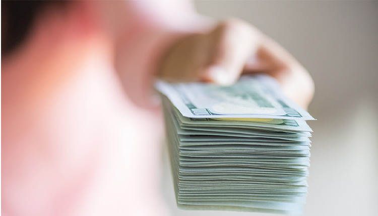 فائدة الأسواق المالية والصورة لفتاة تظهر بيديها وهي ممسكة رزمة من الدولارات